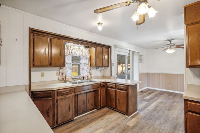 kitchen featuring ceiling fan, sink, light hardwood / wood-style flooring, kitchen peninsula, and ornamental molding