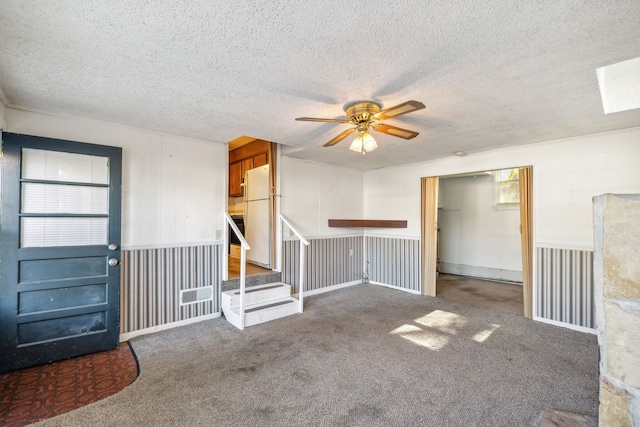 unfurnished living room with wood walls, ceiling fan, dark carpet, and a textured ceiling