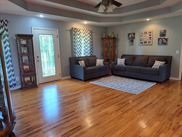 living room with ceiling fan, a tray ceiling, and light hardwood / wood-style floors