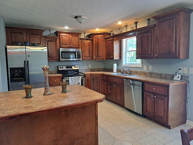 kitchen with appliances with stainless steel finishes, sink, light tile patterned floors, and a textured ceiling