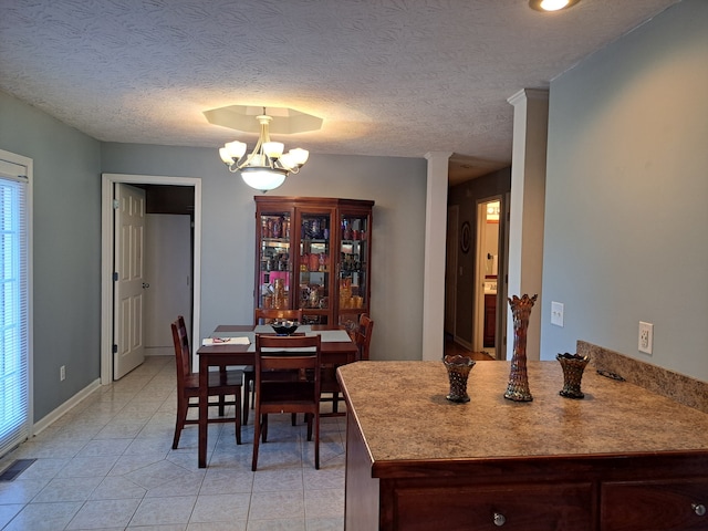 dining room with a textured ceiling, ornate columns, a chandelier, and light tile patterned flooring