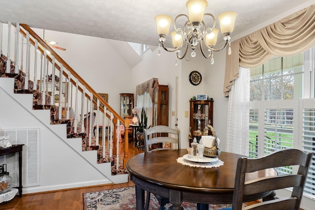 dining space with ceiling fan with notable chandelier, wood-type flooring, a textured ceiling, and lofted ceiling