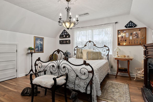 bedroom featuring hardwood / wood-style floors, a textured ceiling, an inviting chandelier, and lofted ceiling