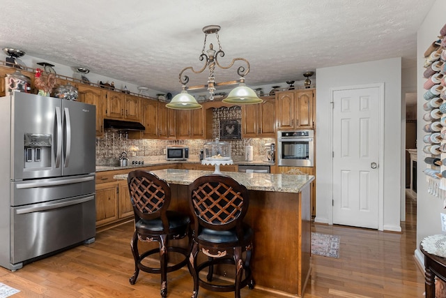 kitchen featuring appliances with stainless steel finishes, a center island, pendant lighting, and wood-type flooring