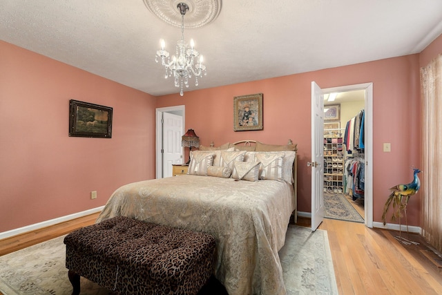 bedroom featuring light wood-type flooring, a walk in closet, a textured ceiling, an inviting chandelier, and a closet