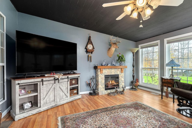 living room featuring wood-type flooring, a stone fireplace, ceiling fan, and wooden ceiling