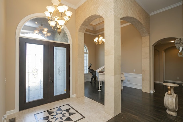 foyer featuring french doors, ornamental molding, a towering ceiling, a notable chandelier, and wood-type flooring