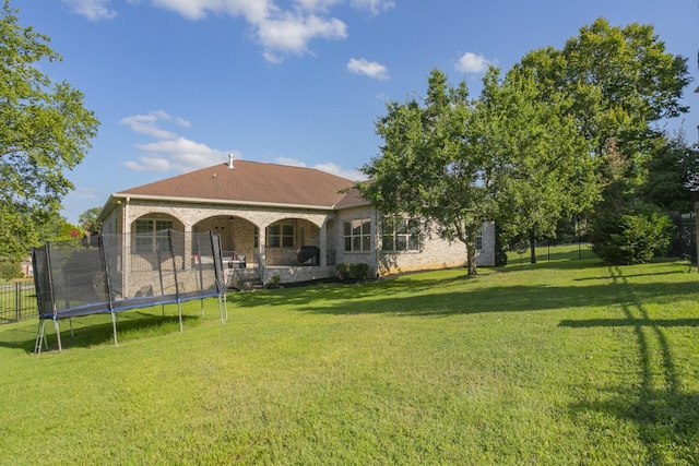 back of house featuring a trampoline and a lawn