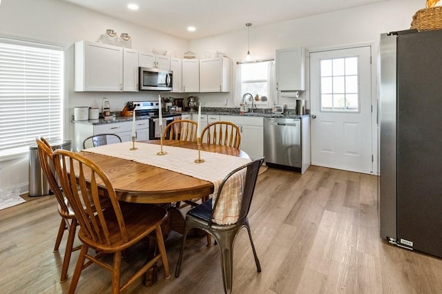 kitchen with sink, light hardwood / wood-style flooring, decorative light fixtures, white cabinets, and appliances with stainless steel finishes