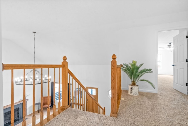 staircase with carpet flooring, a fireplace, ceiling fan with notable chandelier, and vaulted ceiling