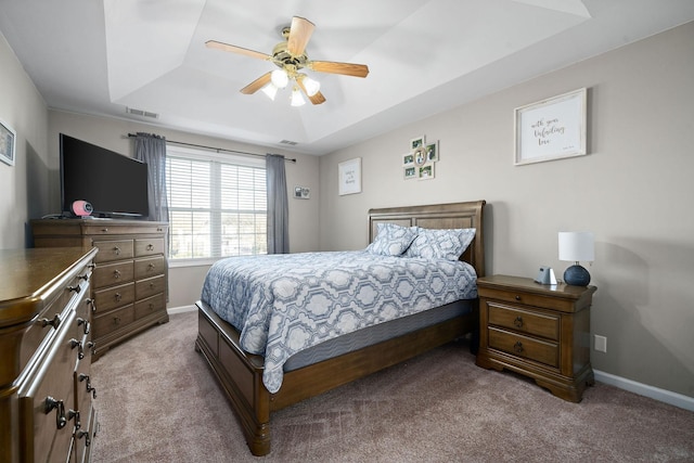 carpeted bedroom with a raised ceiling and ceiling fan