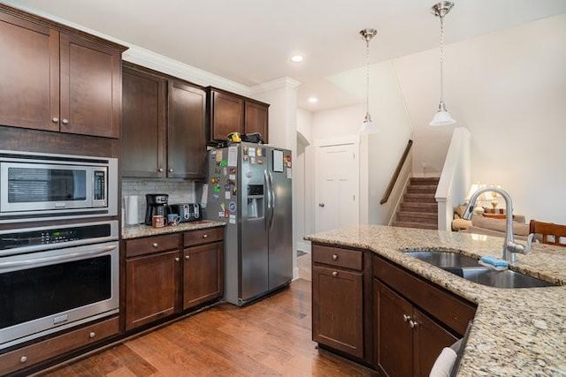 kitchen featuring hardwood / wood-style floors, sink, hanging light fixtures, light stone counters, and stainless steel appliances