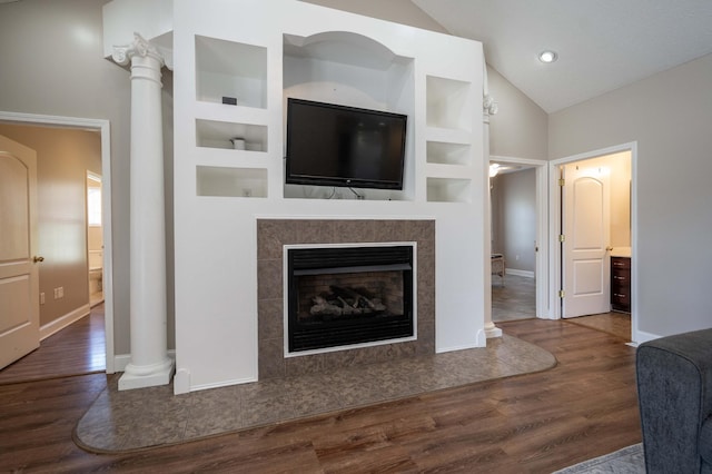 living room featuring built in shelves, a tile fireplace, dark hardwood / wood-style flooring, high vaulted ceiling, and decorative columns