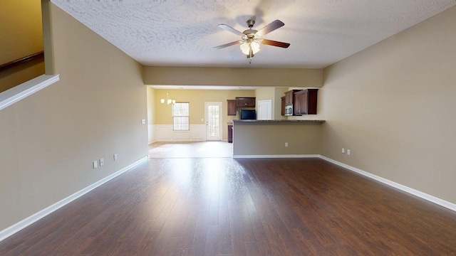 unfurnished living room featuring ceiling fan with notable chandelier, dark hardwood / wood-style flooring, and a textured ceiling