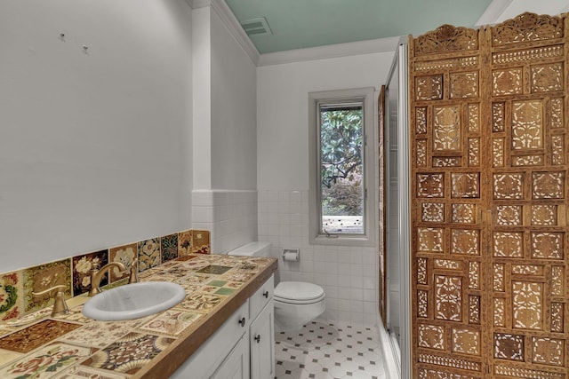 bathroom with vanity, a shower with door, tile patterned flooring, toilet, and tile walls