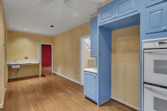 kitchen featuring light wood-type flooring, blue cabinets, double oven, and crown molding