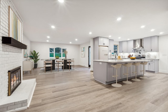 kitchen with gray cabinetry, a kitchen bar, a center island, and wall chimney range hood