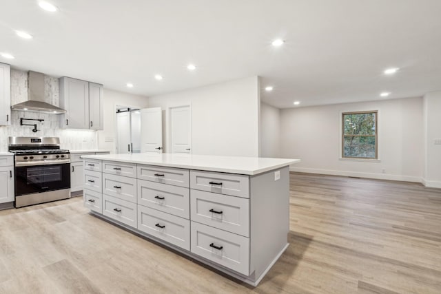 kitchen featuring stainless steel gas range oven, a center island, light hardwood / wood-style flooring, wall chimney range hood, and backsplash