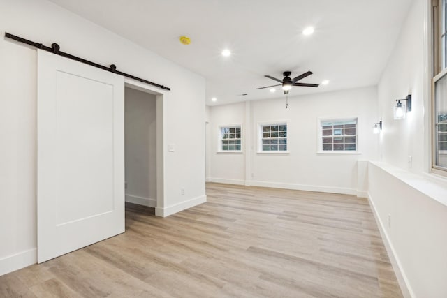 interior space featuring ceiling fan, a barn door, and light hardwood / wood-style floors