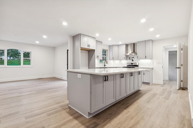 kitchen featuring wall chimney range hood, stainless steel stove, gray cabinets, a kitchen island, and light wood-type flooring