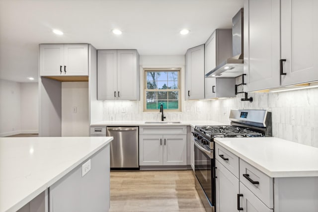 kitchen featuring appliances with stainless steel finishes, tasteful backsplash, sink, wall chimney range hood, and light hardwood / wood-style flooring