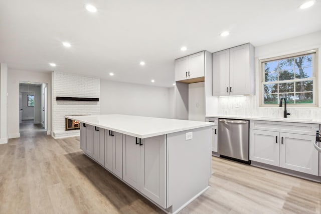 kitchen featuring sink, light wood-type flooring, stainless steel dishwasher, a kitchen island, and decorative backsplash