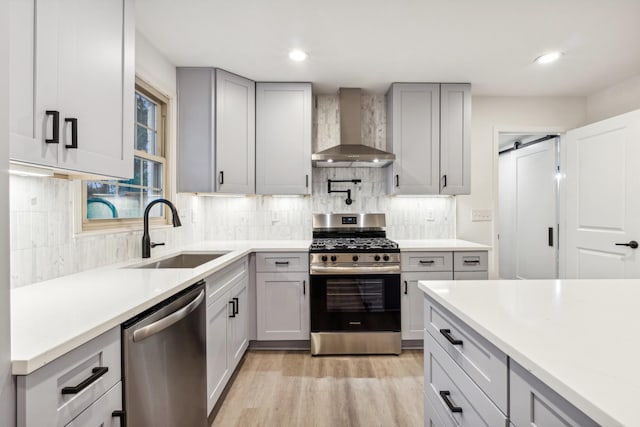 kitchen featuring wall chimney exhaust hood, sink, light hardwood / wood-style flooring, stainless steel appliances, and a barn door