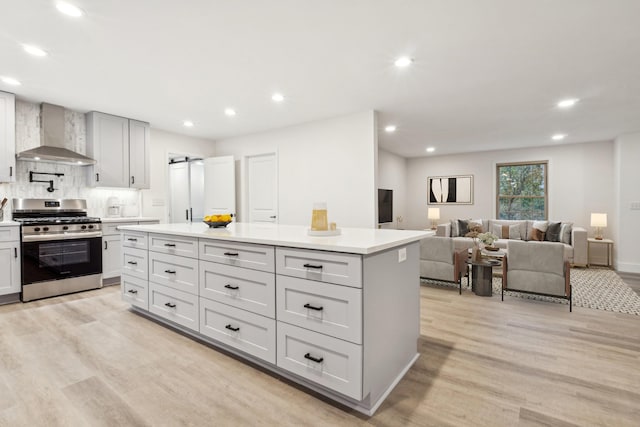 kitchen with decorative backsplash, a center island, gas range, wall chimney range hood, and light wood-type flooring