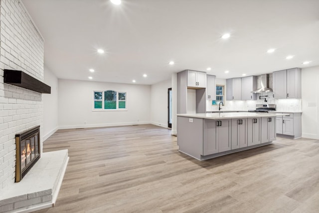 kitchen featuring stainless steel stove, wall chimney exhaust hood, gray cabinets, and a kitchen island with sink