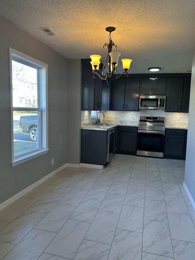 kitchen featuring sink, hanging light fixtures, decorative backsplash, appliances with stainless steel finishes, and a notable chandelier