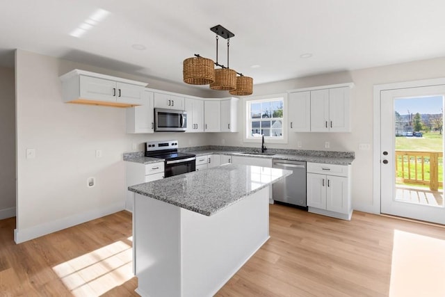 kitchen featuring light stone counters, hanging light fixtures, appliances with stainless steel finishes, a kitchen island, and white cabinets