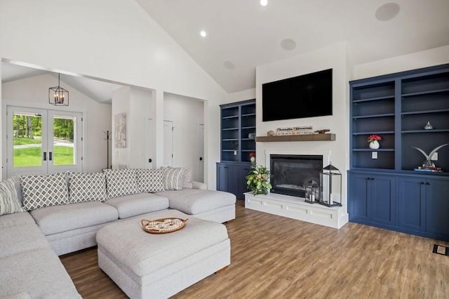 living room featuring a notable chandelier, lofted ceiling, wood-type flooring, and built in shelves