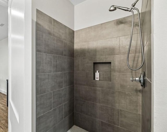 bathroom with a tile shower and wood-type flooring