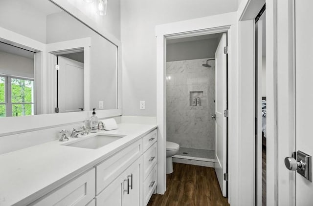 bathroom featuring toilet, wood-type flooring, vanity, and a tile shower