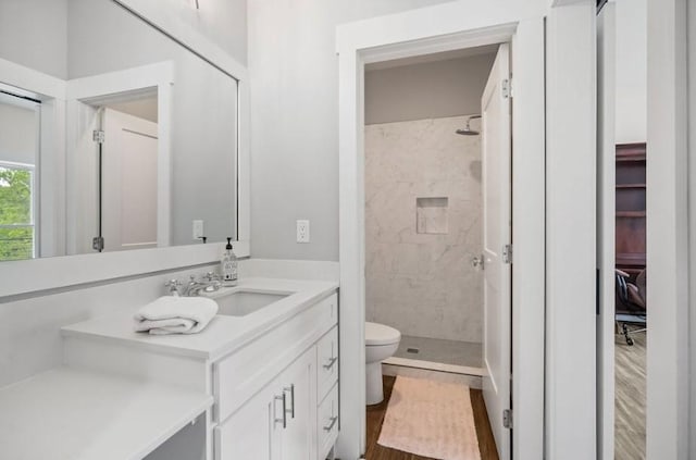 bathroom featuring vanity, toilet, a tile shower, and wood-type flooring