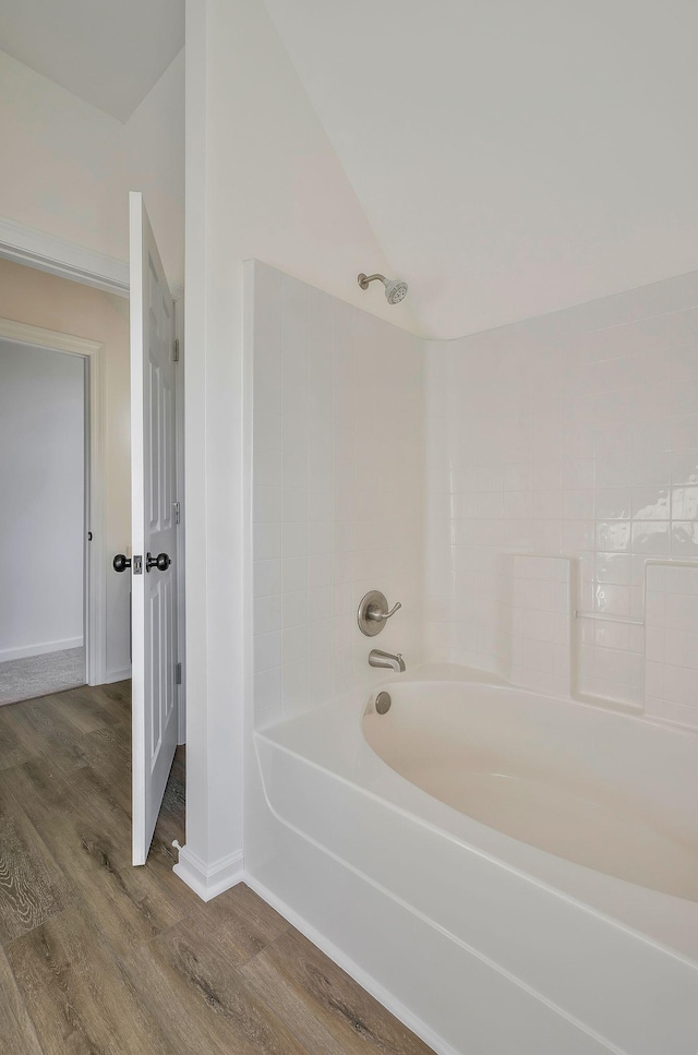 bathroom with hardwood / wood-style floors,  shower combination, and lofted ceiling