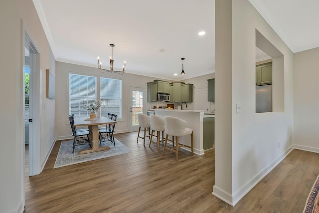 kitchen featuring hanging light fixtures, a kitchen breakfast bar, green cabinetry, wood-type flooring, and ornamental molding