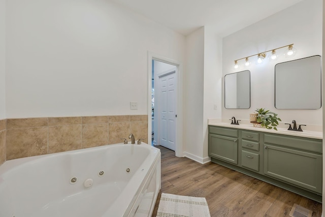 bathroom with hardwood / wood-style flooring, vanity, and tiled bath