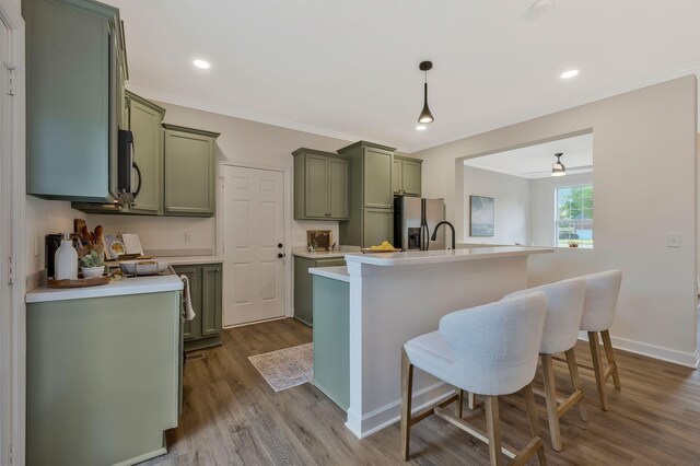 kitchen with green cabinets, wood-type flooring, decorative light fixtures, a kitchen bar, and appliances with stainless steel finishes