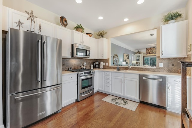 kitchen with backsplash, appliances with stainless steel finishes, pendant lighting, white cabinets, and hardwood / wood-style flooring