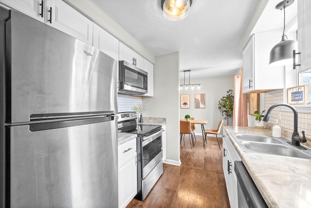 kitchen featuring backsplash, white cabinets, sink, hanging light fixtures, and stainless steel appliances