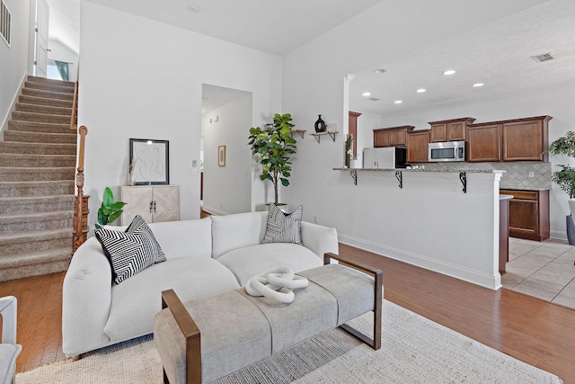 living room featuring stairs, light wood finished floors, and visible vents