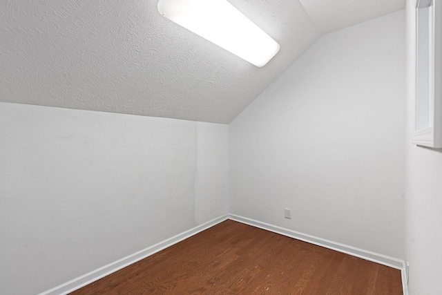 additional living space with dark wood-style floors, baseboards, vaulted ceiling, and a textured ceiling