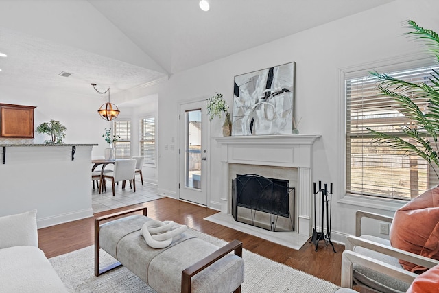 living area featuring vaulted ceiling, wood finished floors, a high end fireplace, and an inviting chandelier