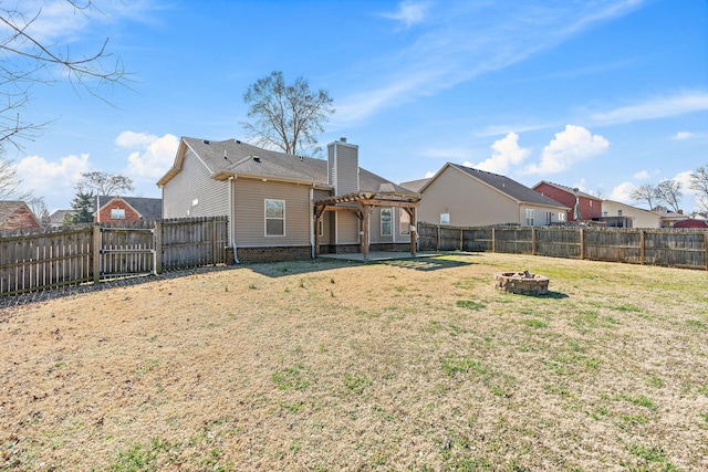 back of property featuring a fenced backyard, a fire pit, a yard, a pergola, and a chimney