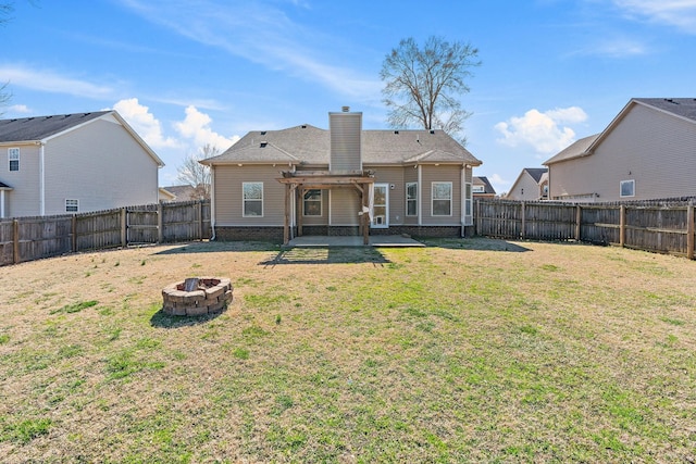 rear view of house with an outdoor fire pit, a chimney, a lawn, and a fenced backyard