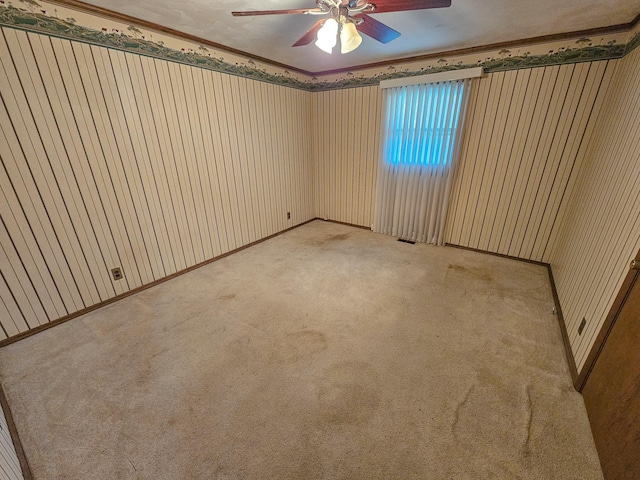 carpeted spare room featuring ceiling fan, wood walls, and ornamental molding