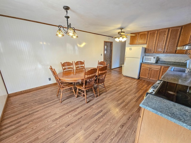 dining area with hardwood / wood-style flooring, ceiling fan with notable chandelier, ornamental molding, and sink