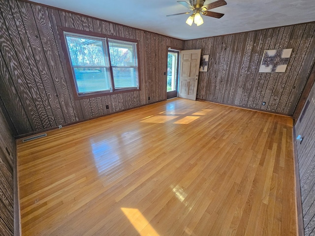 spare room featuring ceiling fan, wood walls, and light wood-type flooring