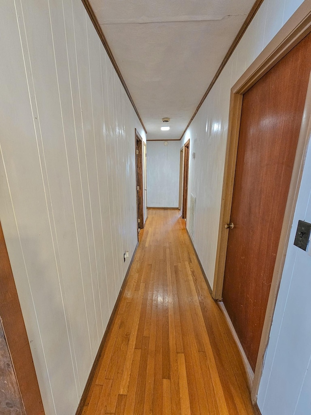 hall featuring light hardwood / wood-style flooring, ornamental molding, and wood walls